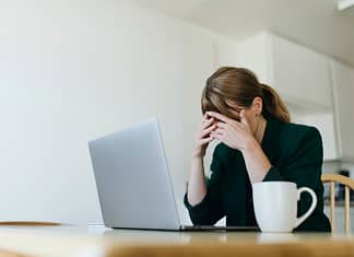 Woman sitting across from laptop with hands over her eyes - Actions to overcome job search blues