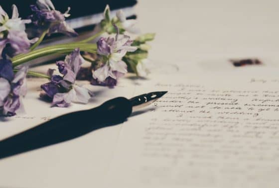 Fountain pen on top of a writing pad next to a bouquet of flowers - Myths About Blogging Before Starting A Blog