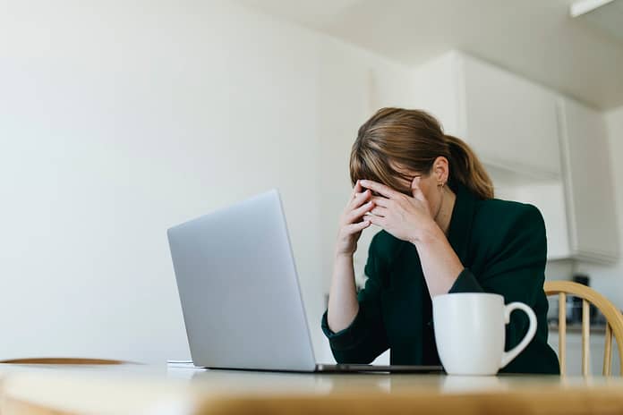 Woman sitting across from laptop with hands over her eyes - Actions to overcome job search blues