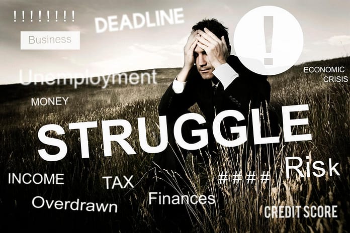 Businessman sitting in a field with hands on his face and words of struggle, deadline, finances, etc. printed all over