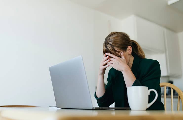 Woman sitting across from laptop with hands over her eyes - Actions to overcome job search blues