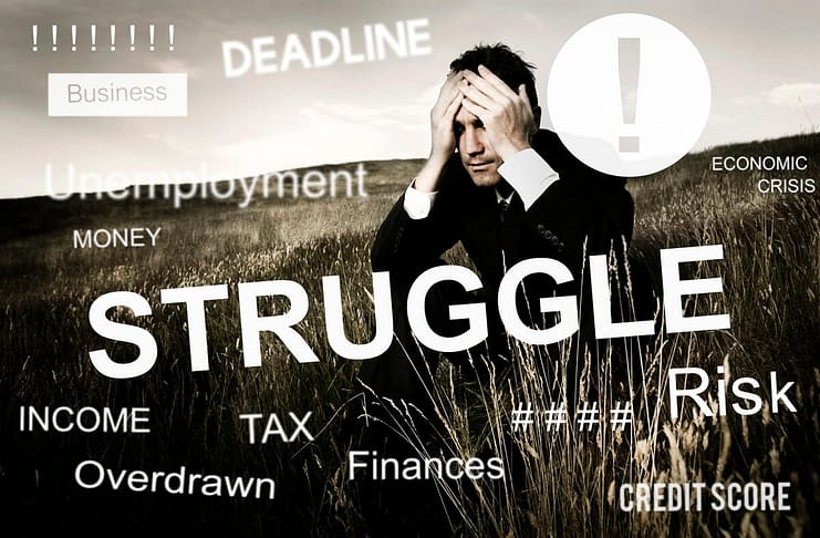 Businessman sitting in a field with hands on his face and words of struggle, deadline, finances, etc. printed all over