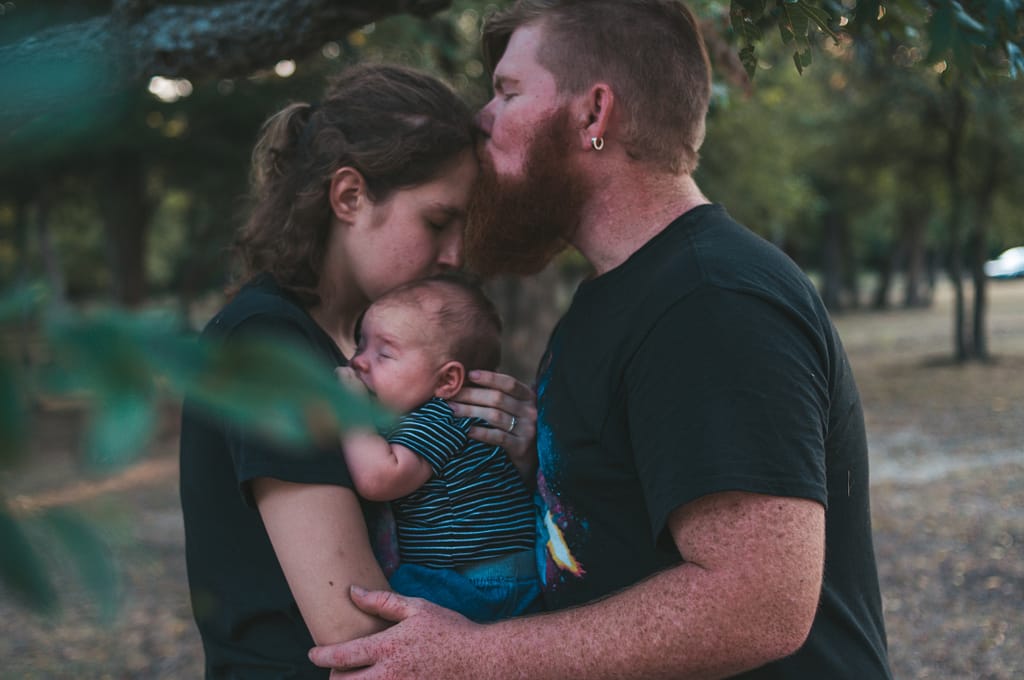 A husband is lovingly kissing his wife, who's holding their baby - 11 Simple Ways to Be Your Very Best