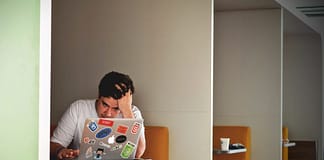 Man sitting in a booth looking at his computer, overwhelmed, with hand on his head. Overcome The Feeling Of Overwhelm
