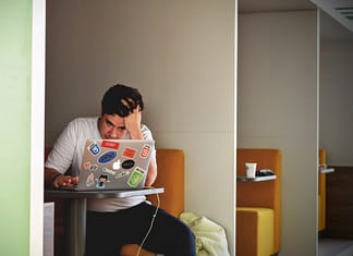 Man sitting in a booth looking at his computer, overwhelmed, with hand on his head. Overcome The Feeling Of Overwhelm